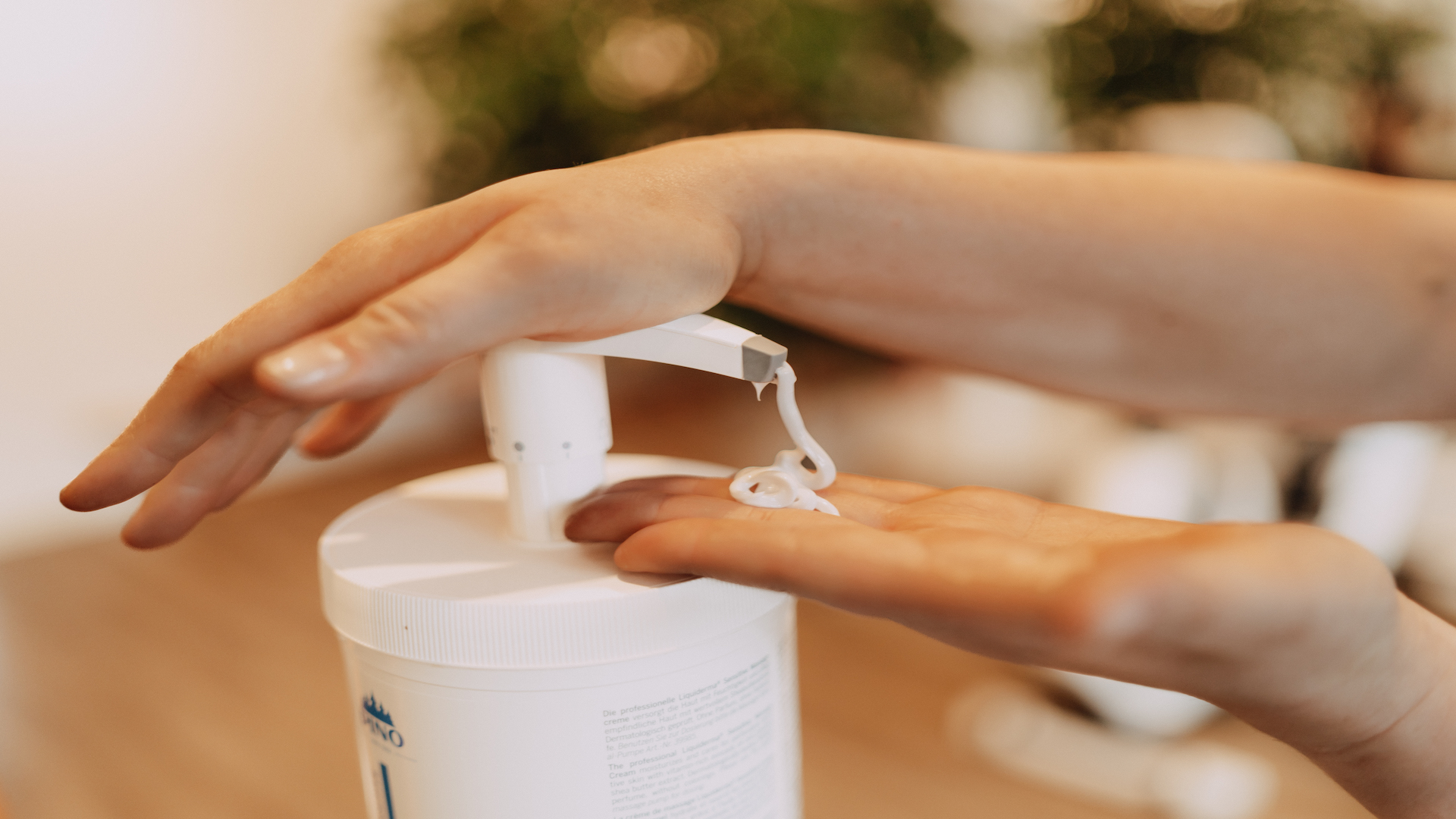 Hände beim Drücken eines Spenders mit Massage-Lotion